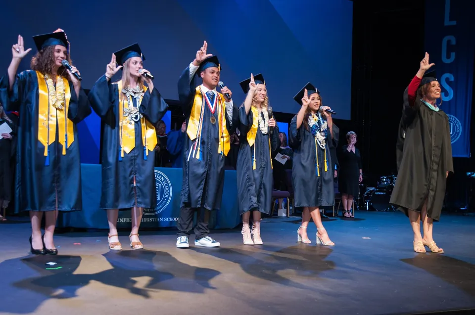 I diplomati della Linfield Christian School sono su un palco e festeggiano il loro diploma indossando toge gialle e nere.