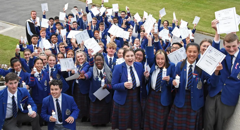 Un grande gruppo di studenti del St. Kevin’s College in divisa scolastica tiene in mano cartelli e fogli durante un'assemblea all'aperto.
