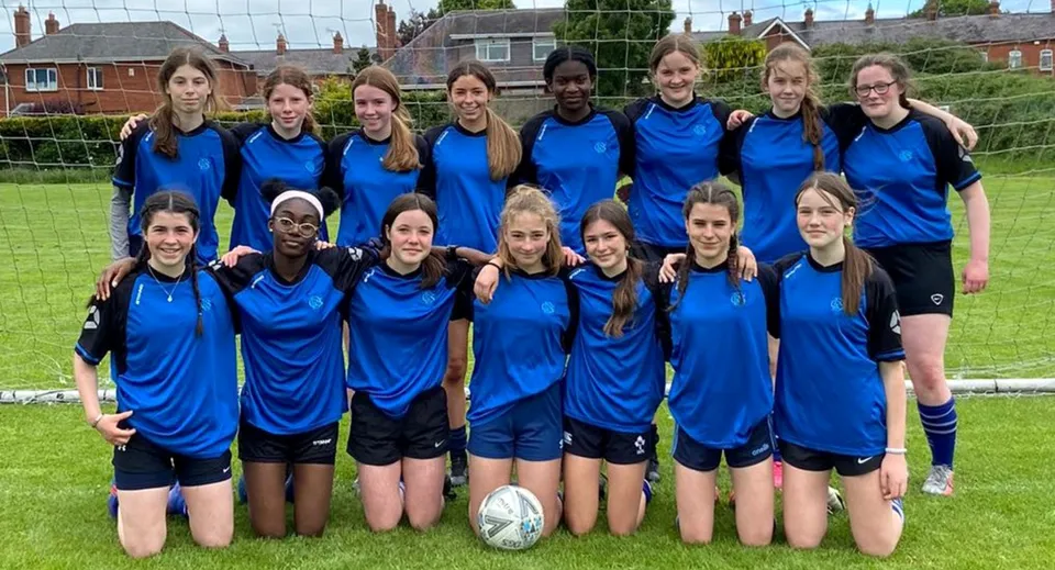 Un gruppo di studentesse della Dundalk Grammar School si trova insieme su un prato davanti a edifici e alberi.