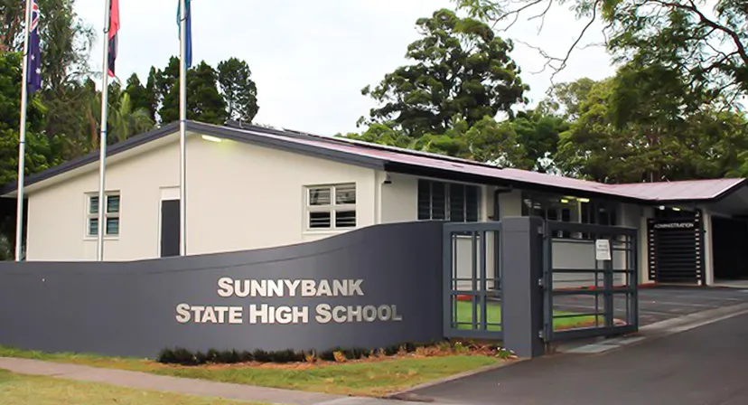 L'edificio scolastico moderno della Sunnybank State High School è circondato da alberi verdi.