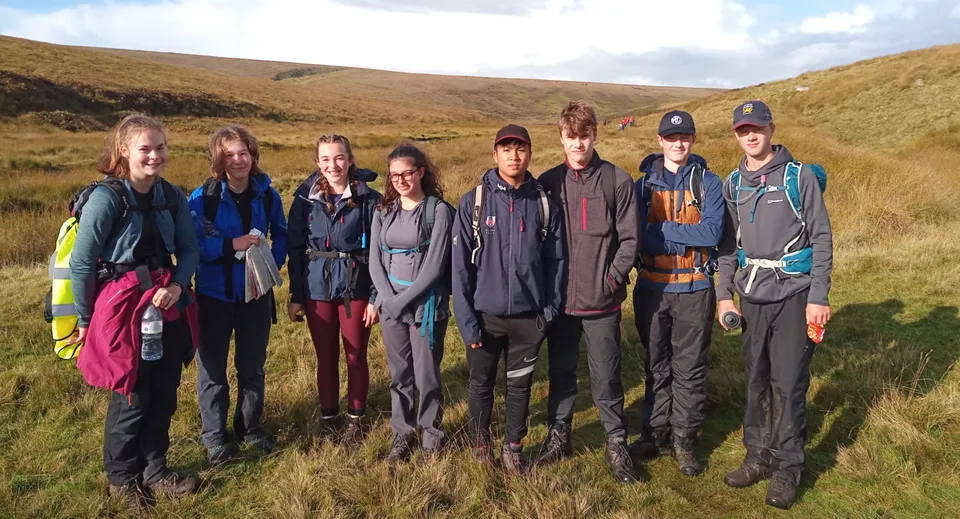 Un gruppo di studenti e studentesse della Mount Kelly School all'aperto in un paesaggio collinare sotto un cielo nuvoloso.
