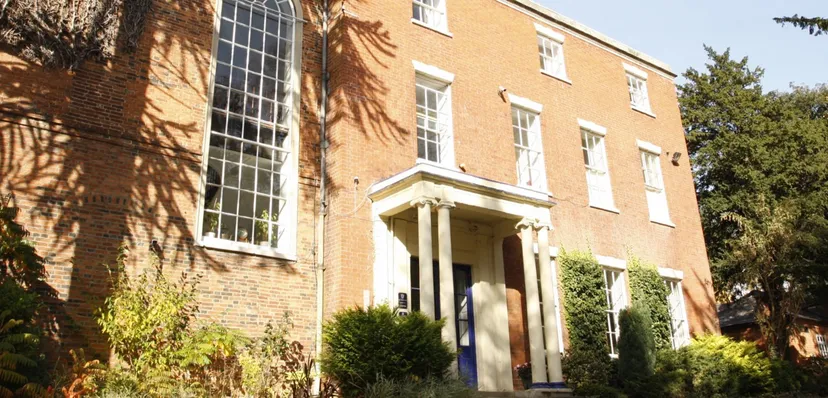 L'edificio in mattoni con grandi finestre e un ingresso caratteristico nel campus del Brooke House College è circondato da aree verdi.