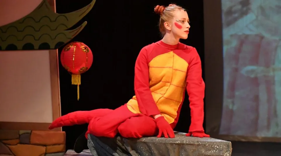 Una persona in costume rosso e giallo si trova sul palco della Saint Edward's School con lanterne cinesi sullo sfondo.