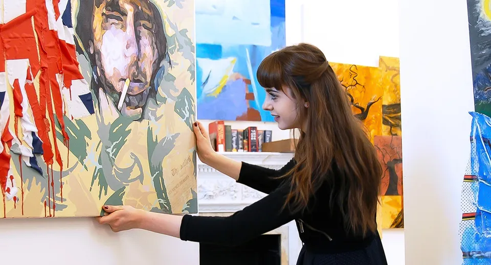 Una studentessa di MPW Birmingham tiene un grande dipinto contro una parete nell'aula d'arte.