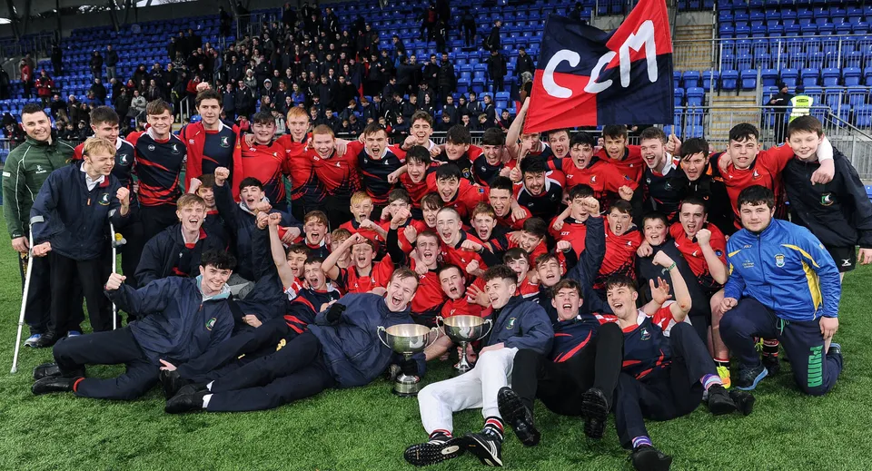 Un gruppo di studenti del Columba College in divisa rossa si riunisce sul campo da gioco con una bandiera rossa.