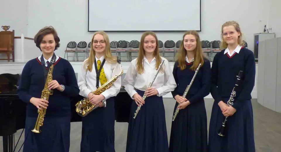Cinque studentesse in divisa scolastica della Stamford Endowed Schools sono in piedi insieme a una flautista davanti a uno schermo di proiezione.