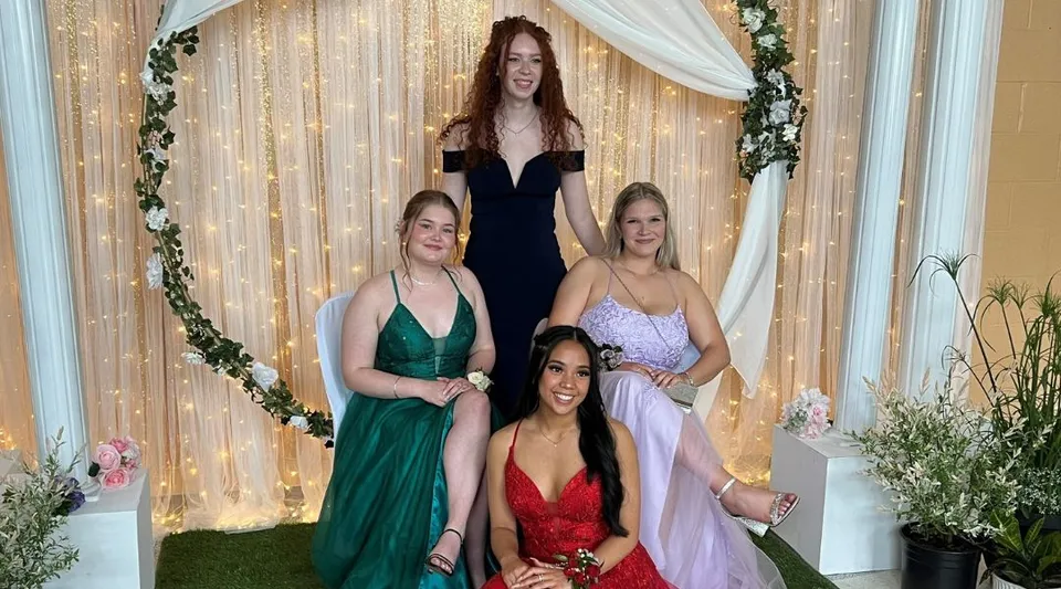 Quattro giovani donne in abito elegante posano insieme davanti a uno sfondo decorativo nel campus del Smiths Falls District Collegiate Institute.