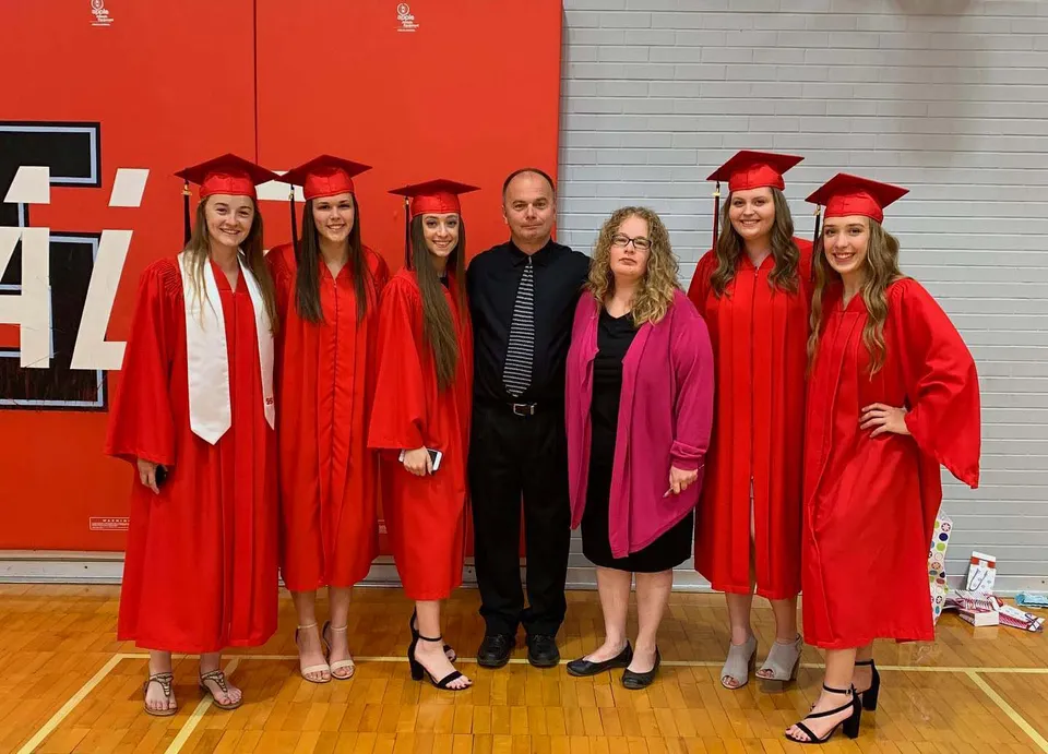 Un gruppo di studenti della Lambton Kent Composite School è in piedi davanti a una parete rossa indossando toghe rosse da diploma.