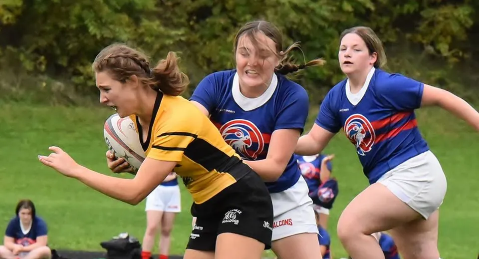 Tre studentesse del St. Finian’s College Mullingar fanno sport su un campo erboso con alberi sullo sfondo.