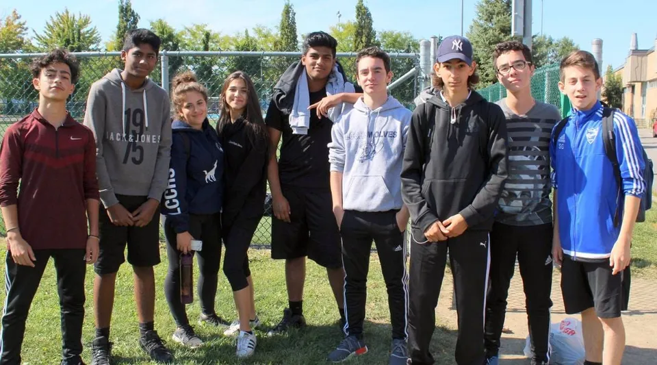 Un gruppo di studenti e studentesse si trova su un prato verde davanti agli edifici del campus della LaSalle Community Comprehensive High School.