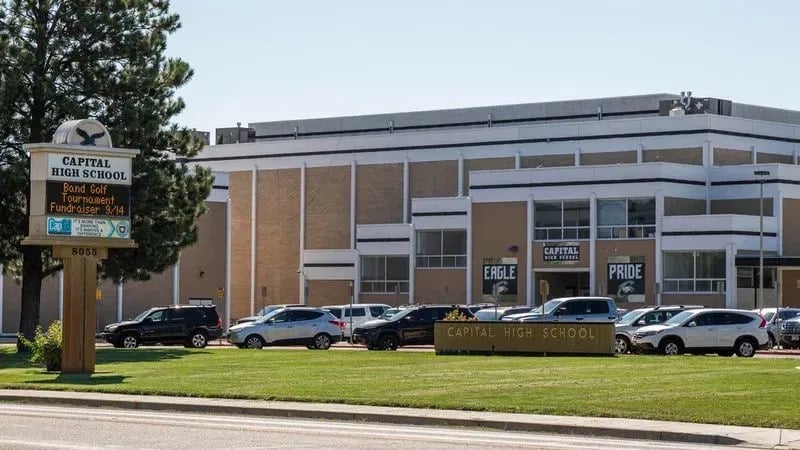 Das Gebäude der Capital High School mit Schulschild und Parkplatz unter blauem Himmel