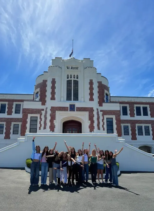 Gruppo di studentesse che festeggia con le braccia alzate davanti a un edificio scolastico storico in Nuova Zelanda