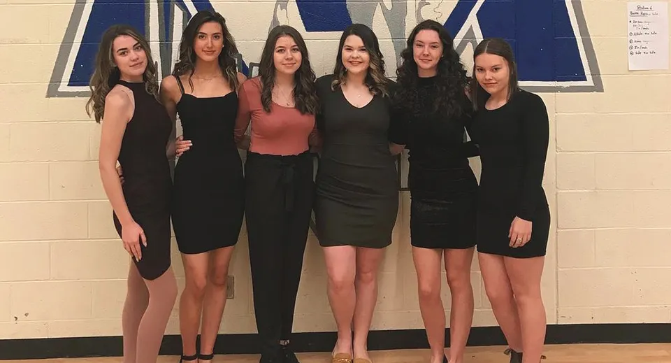 Sei studentesse della St. Kevin's High School con outfit nero-rossi davanti a uno sfondo blu e bianco.
