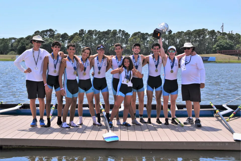 Un gruppo di studenti della Miami Beach Senior High School si trova insieme come squadra di canottaggio su una passerella vicino all'acqua.