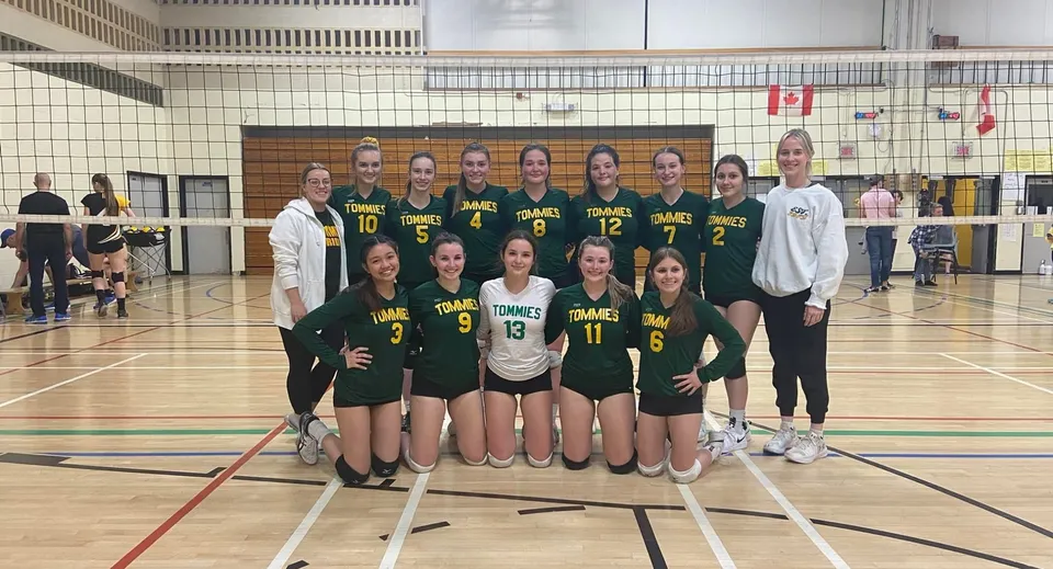 Un gruppo di pallavoliste in maglia verde posa sul campo da pallavolo della James M. Hill Memorial High School.