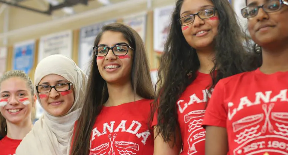 Un gruppo di giovani donne con magliette rosse con la scritta Canada posa insieme negli spazi interni della Bradford District High School.