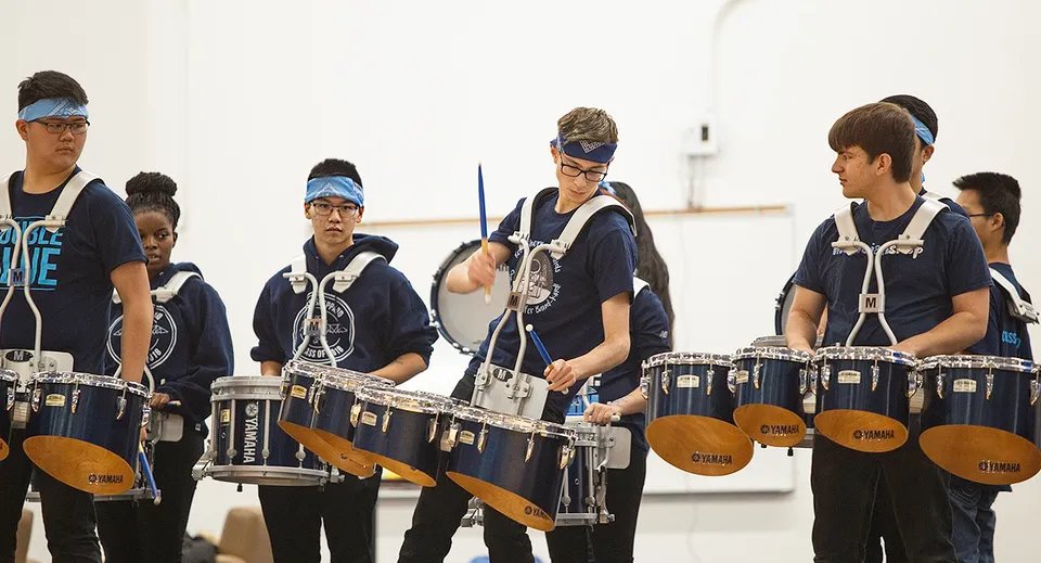 Studenti della Ross Sheppard High School si esercitano insieme con strumenti a percussione in uno spazio interno luminoso.