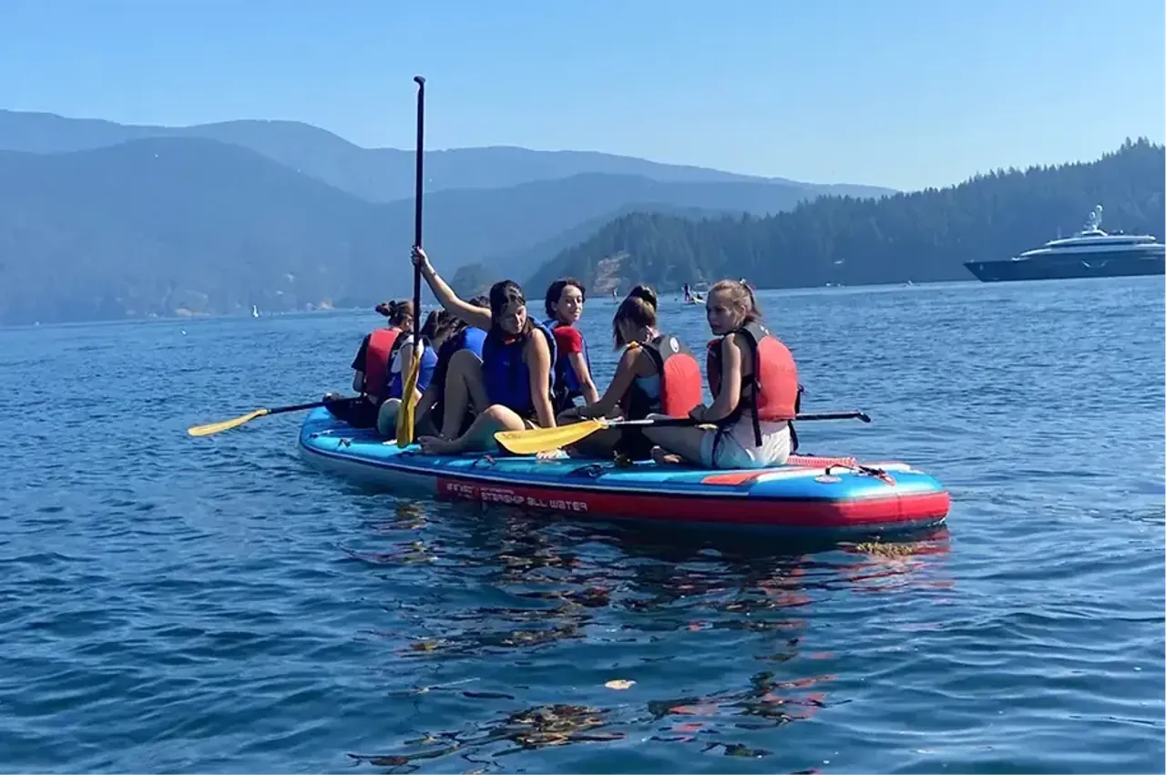 Gruppo di studenti su una grande tavola SUP in un lago tra le montagne