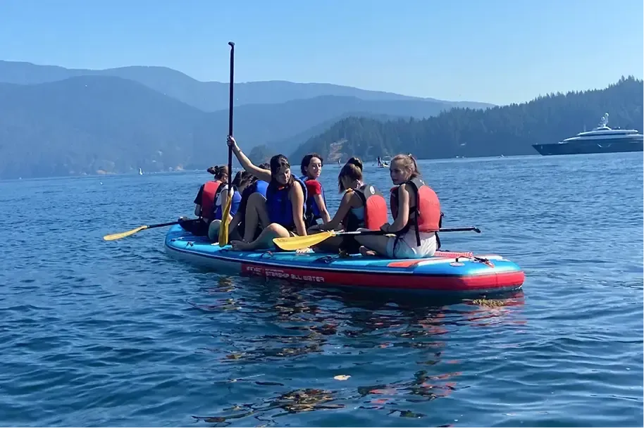 Gruppo di studenti su una grande tavola SUP in un lago tra le montagne