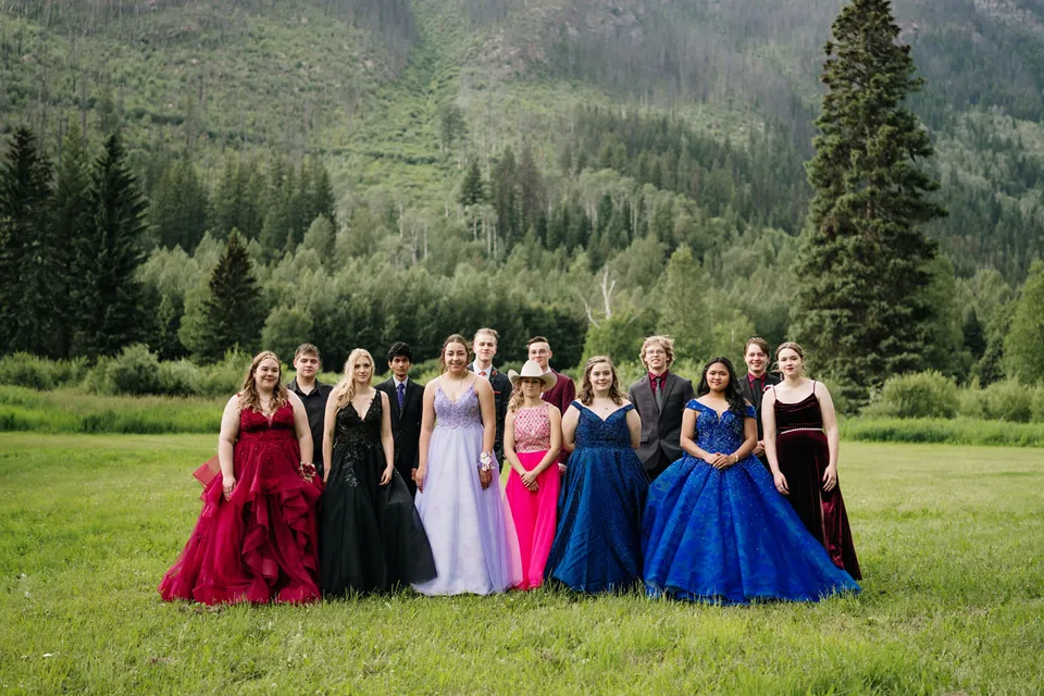 Un gruppo di giovani studentesse in abiti colorati si trova nel paesaggio montano boscoso sul terreno della Valemount Secondary School.
