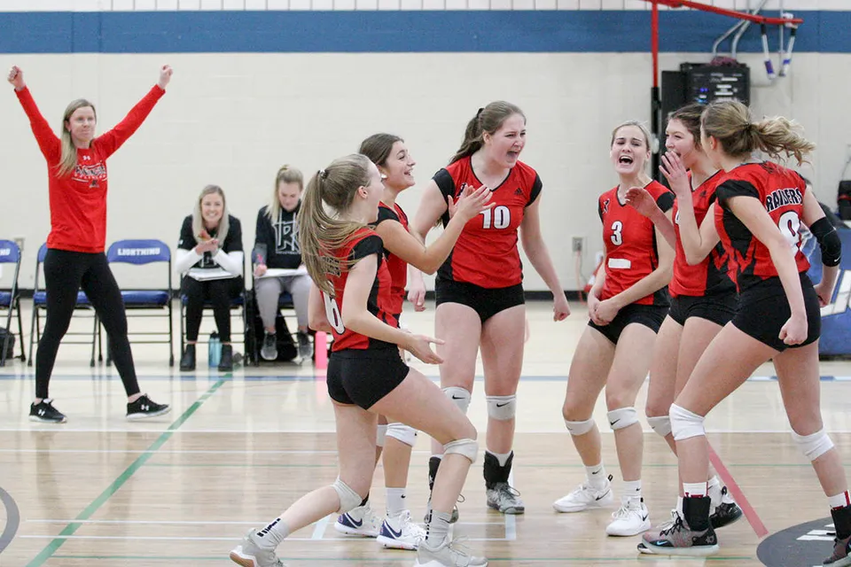 Studentesse della Lindsay Thurber Comprehensive High School festeggiano insieme sul campo da pallavolo durante una partita.
