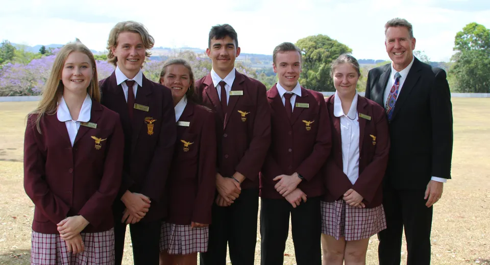 Un gruppo di studenti della Atherton State High School sta in piedi su un campo erboso davanti ad edifici e alberi.