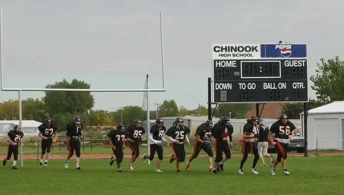 Un grupo de futbolistas uniformados corre por el campo de Chinook High School frente a la grada.