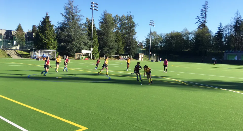 Studenti della Prince of Wales Secondary School giocano a calcio sul campo in erba sintetica con alberi ed edifici sullo sfondo.