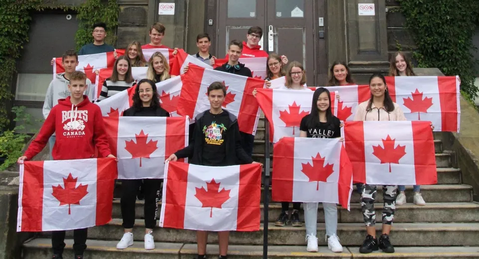 Studenti della Harbour View High School sono sulle scale di un edificio e tengono grandi bandiere canadesi.