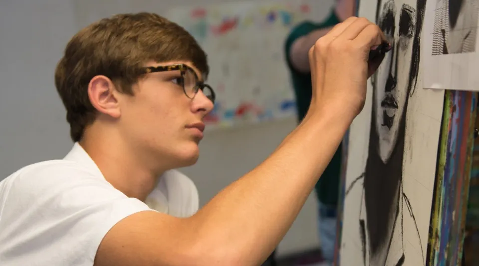 Un ragazzo con gli occhiali è in piedi davanti a una parete con opere d'arte colorate nel campus della Woodberry Forest School.
