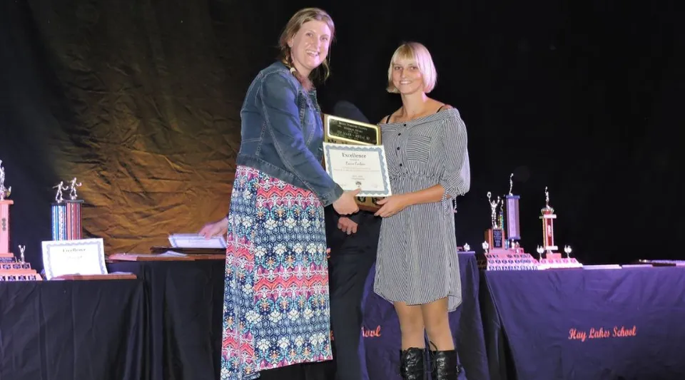 Due persone sono sul palco della Hay Lakes School e tengono insieme un premio.