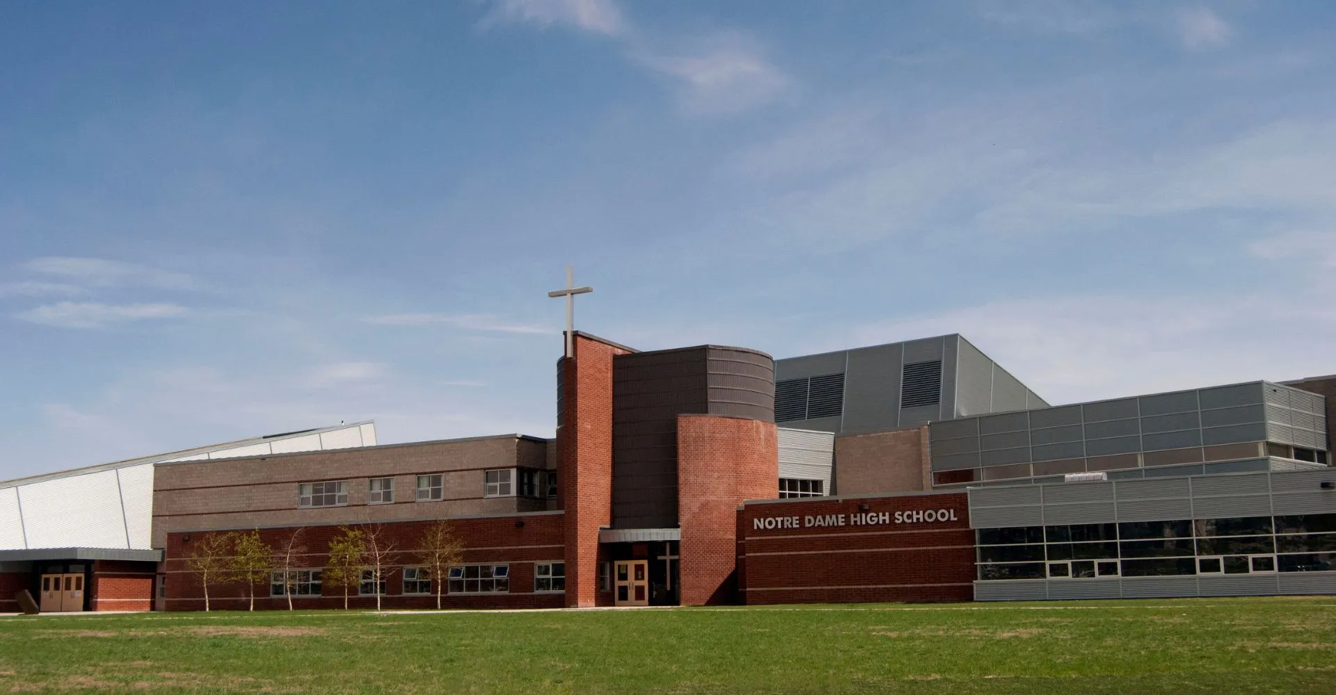 L'edificio scolastico moderno a più piani della Notre Dame High School a Calgary con facciata in mattoni e ampie finestre sotto un cielo limpido.