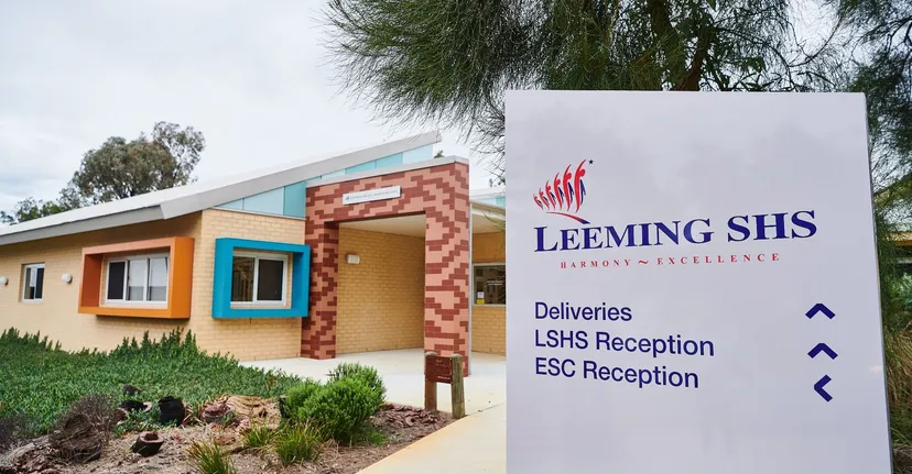 L'edificio moderno a un piano della Leeming Senior High School, con facciata in mattoni e cartello con il nome della scuola, è circondato da alberi e cespugli.