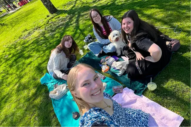Ragazze fanno un picnic su un prato con un cagnolino bianco, selfie al sole