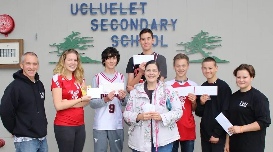 Studenti e collaboratori della Ucluelet Secondary School posano insieme davanti a un corridoio della scuola mostrando dei certificati.