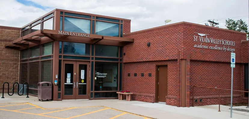 L'edificio in mattoni con l'ingresso principale delle St. Vrain Valley Schools si trova sotto un cielo nuvoloso ed è circondato da un'area pavimentata.