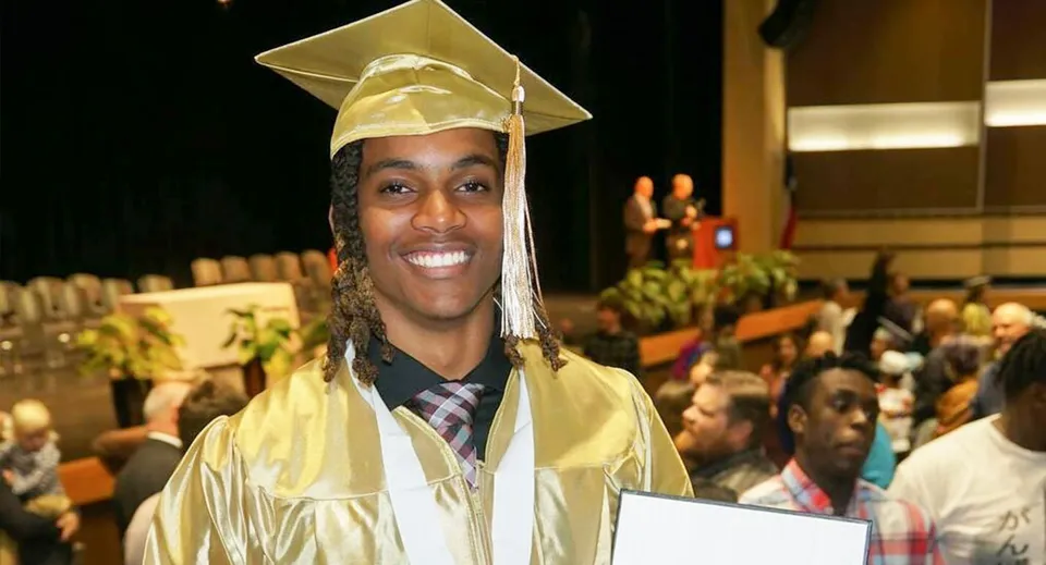 Un giovane in toga da diploma tiene in mano un diploma nell'aula magna affollata nel campus della Three Oaks Senior High.
