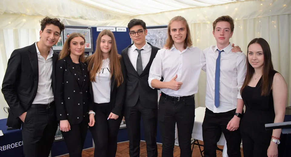 Un gruppo di studenti in abito formale posa davanti a una tenda bianca nel campus del D'Overbroeck's College.