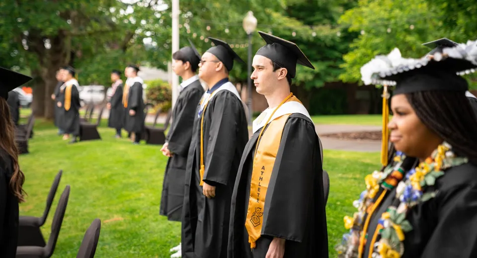 Un gruppo di diplomati della Mannahouse Christian Academy in abito accademico su un prato del campus.