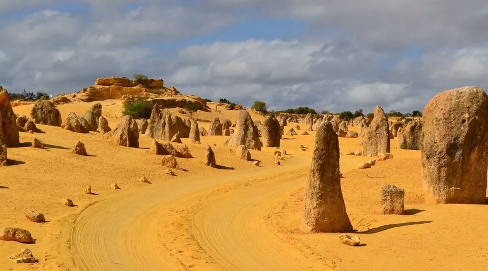 Un vasto paesaggio desertico con alte formazioni rocciose e un sentiero tortuoso sotto un cielo nuvoloso.