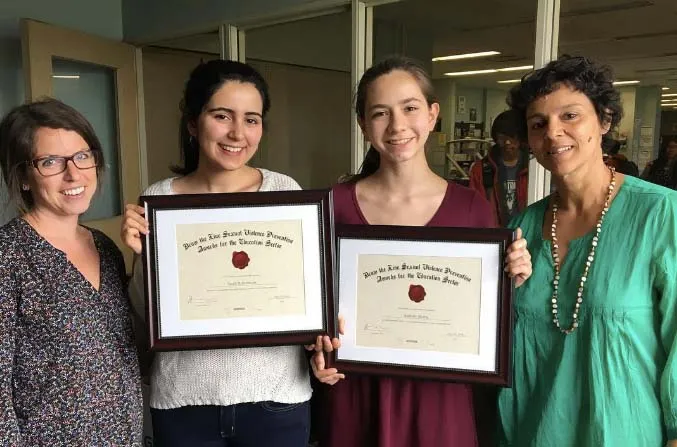 Cuatro mujeres del Bloor Collegiate Institute sostienen juntas certificados enmarcados en un espacio interior.