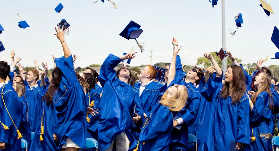 Un gruppo di diplomati della Sioux Falls Christian School lancia in aria i tocchi blu davanti a un cielo limpido.