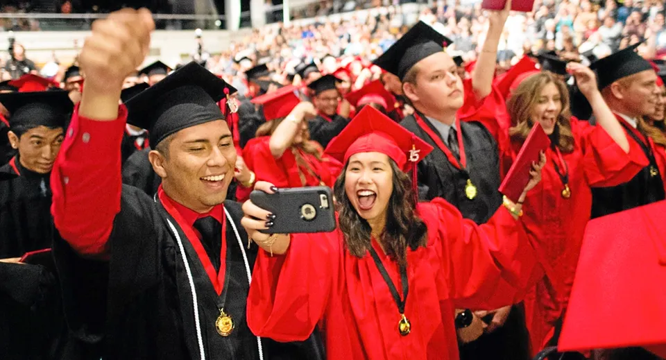 Un grande gruppo di diplomati della Gladstone Secondary School festeggia il diploma in toghe rosse e scatta dei selfie.