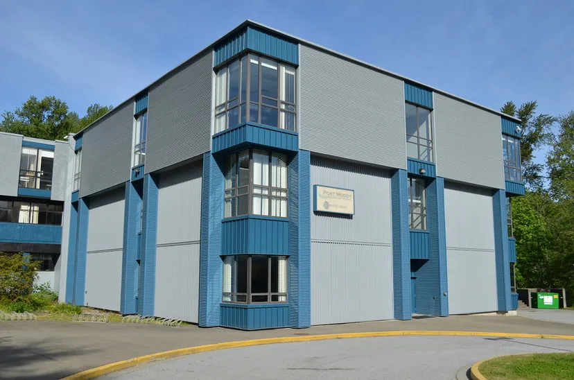 L'edificio moderno a più piani della Port Moody Secondary School con facciata grigia e dettagli blu è circondato da alberi.