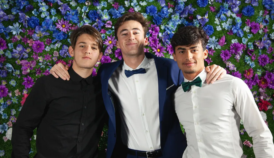 Tre studenti della Layton Christian Academy posano insieme davanti a uno sfondo di fiori colorati.
