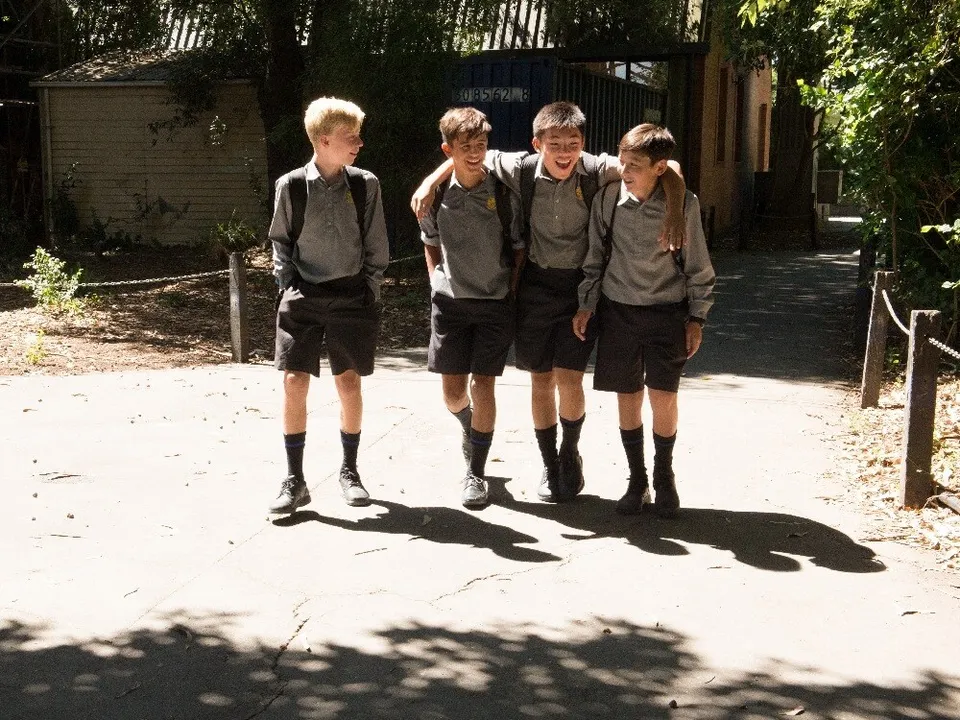 Un gruppo di studenti si trova all'esterno nel campus della Christchurch Boys High School vicino a un sentiero in ghiaia e cespugli.