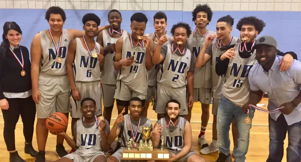 Un gruppo di studenti della Notre Dame High School festeggia insieme la vittoria di un torneo di basket con una coppa.