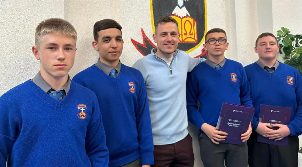 Un gruppo di studenti della St. Vincent's Secondary School a Dublin in piedi davanti a una parete con uno stemma.