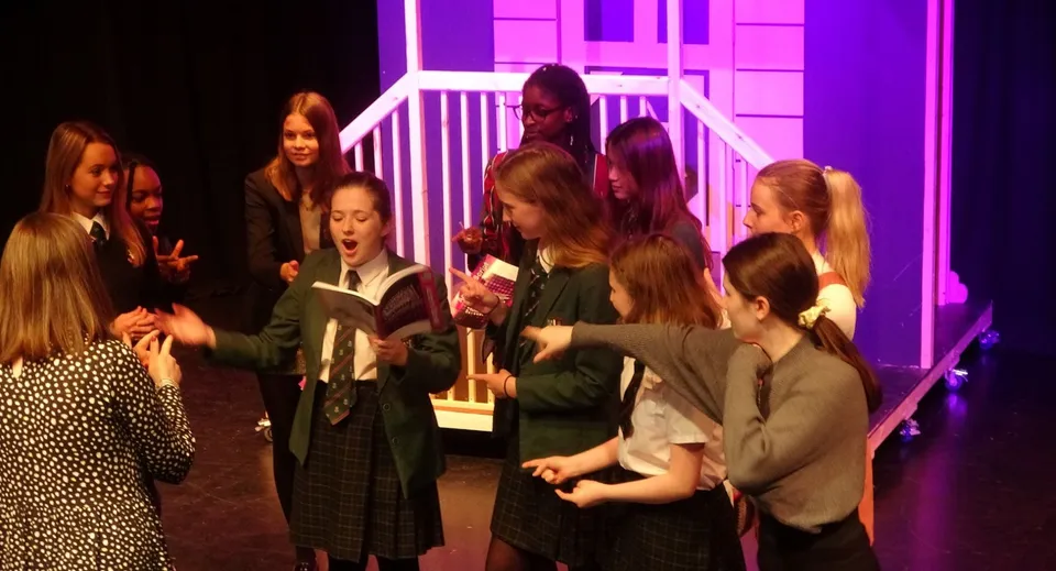 Un gruppo di studenti della Woodbridge School si trova su un palco con luci colorate all'interno della sala teatro.
