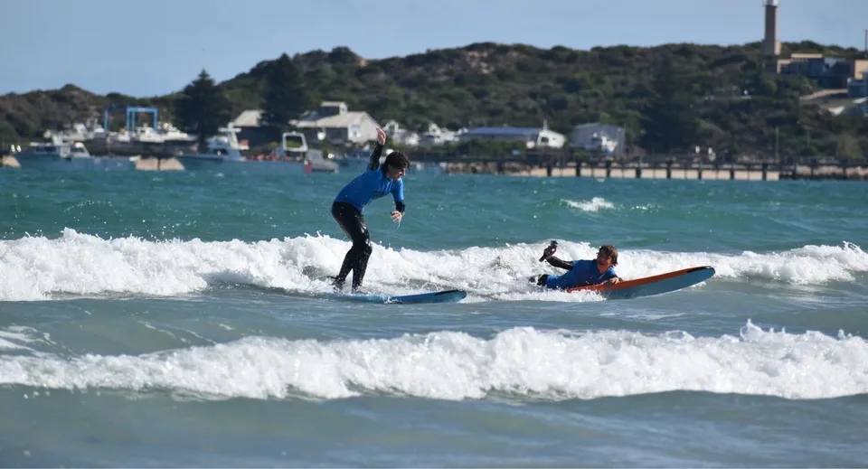 Uno studente della Pembroke School fa surf sulle onde davanti a una pittoresca città costiera.
